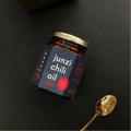 Jar of junzi chili oil with a gold spoon on a black background